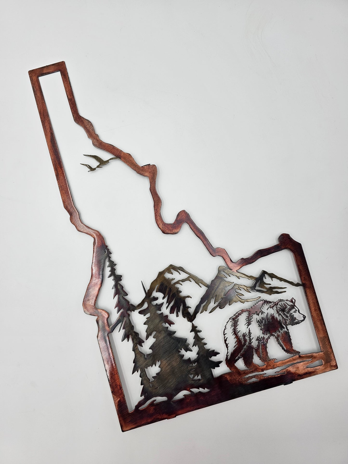 Idaho state sign with bear and mountain scene. Measures 20.5 Inches High x 12 Inches Wide x 18 Gauge. Comes in five colors, Colored-Rustic, Flat Black, Hammered Black, Hammered Beige, and Bare Metal. Made from cold rolled 18 gauge sheet metal. Sprayed with automotive clear coat. If you want to hang this outside in the elements let us know in the personalization box and we'll spray the back of it for you.