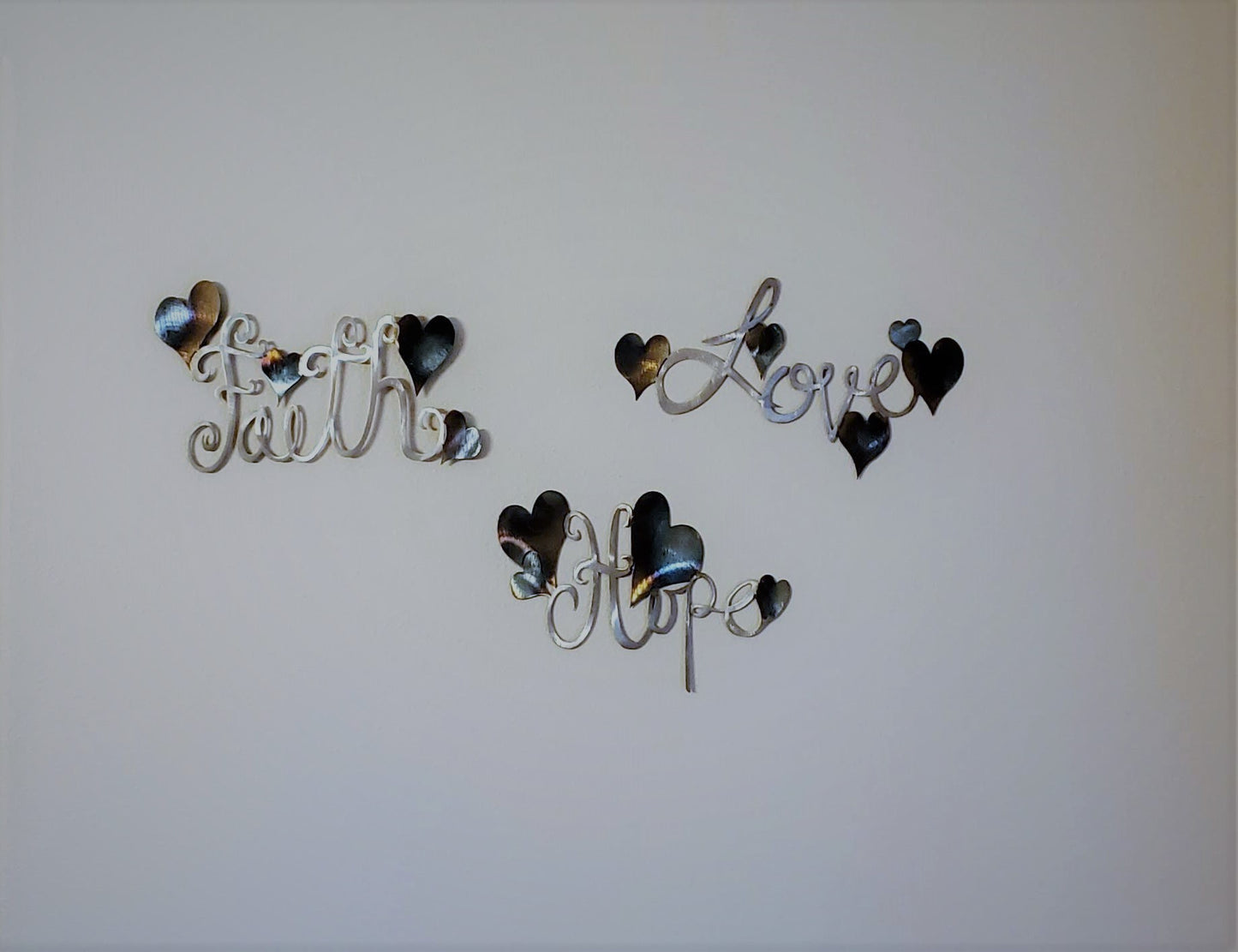 Faith Hope Love Metal Wall Hanging Words with colorful hearts on each word. Largest one measures 6 1/2 inch High by 11 3/8 inches wide by 18 gauge. Made from 18 gauge cold rolled sheet metal. Available in four colors. Colored which is very rustic looking, black, hammer tone, and bare metal. Sprayed with a layer of varathane. Hangs via nails not included. These can be hung together or separate.