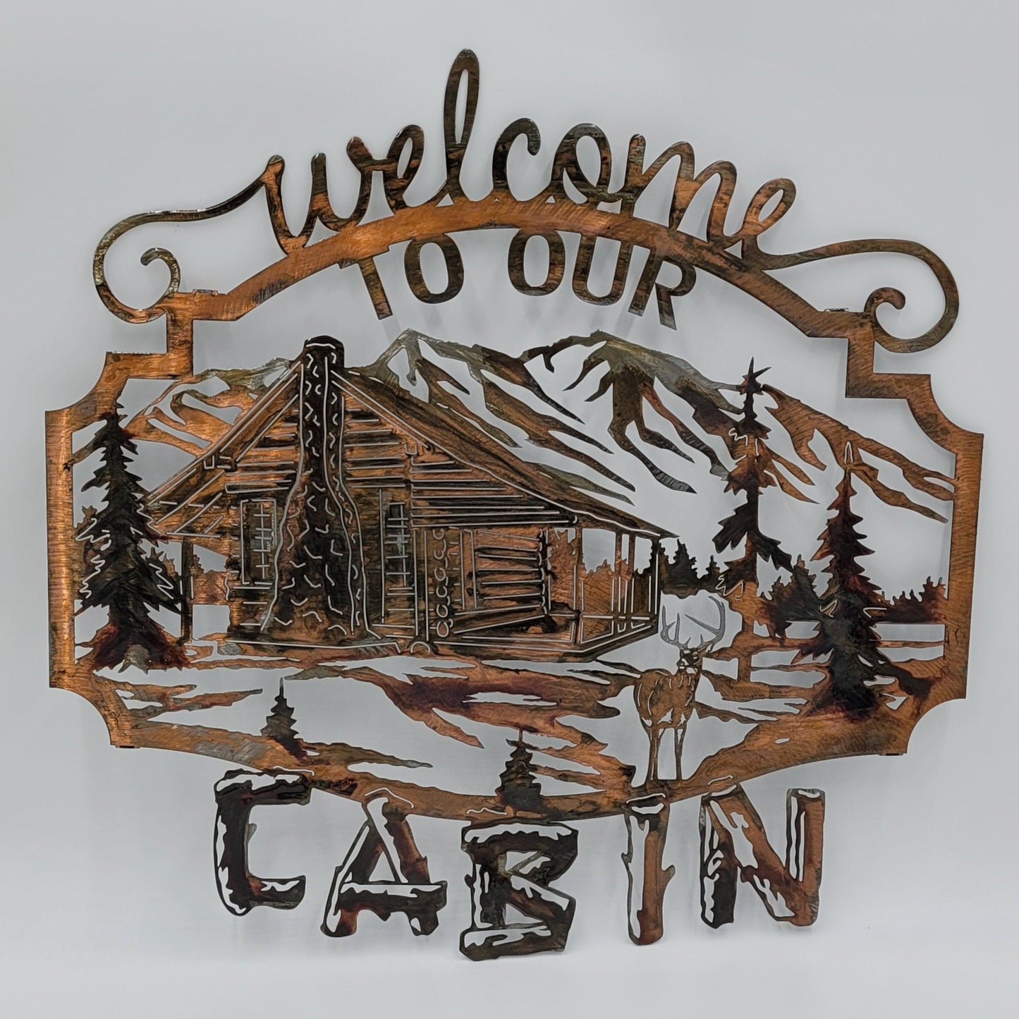 Welcome To Our Cabin White Tail Deer Sign features a rustic log cabin nestled into a mountain scene background surrounded by by trees, and a white tail deer standing in front of the scene. Measures 19.5 Inches High x 20 Inches Wide x 18 gauge. Available inf four colors; Colored-Rustic, Black, Hammer Tone, Bare Metal. This is the Colored-Rustic version. Gift Wrapping available at check out.