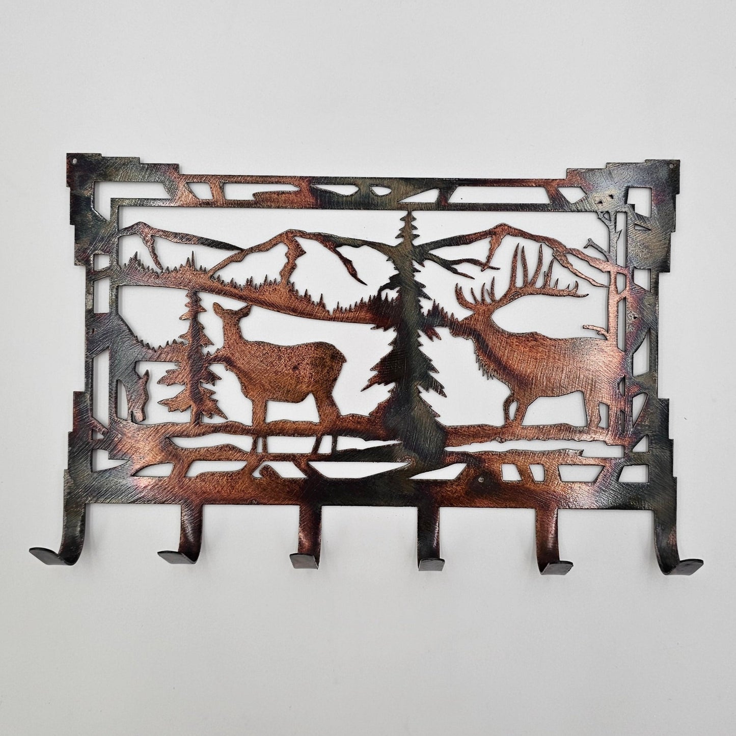 Southwest Style Rustic Elk Key Rack features a male and female elk in a mountain scene background. Measures 8" Wide x 5.5" High. Has 6 hooks for keys. Hangs via two nails not included. Available in four colors; Colored-Rustic, Black, Hammer Tone, Bare Metal. This is the colored version. Sprayed with a thick layer of Varathane. Gift Wrapping available at checkout.