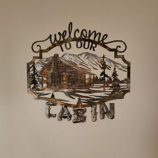 Welcome To Our Cabin Metal Wall Hanging features a log cabin with a mountain background. There's trees and snow in the front yard. There's wording that reads welcome to our on top and the word cabin on the bottom. Measures19 1/2 inches high by 20 inches wide by 18 gauge. Made from cold rolled 18-gauge sheet metal. Available in four colors. Colored which is very rustic looking, black, hammer tone, and bare metal. Sprayed with a layer of varathane. Gift wrapping available at checkout.