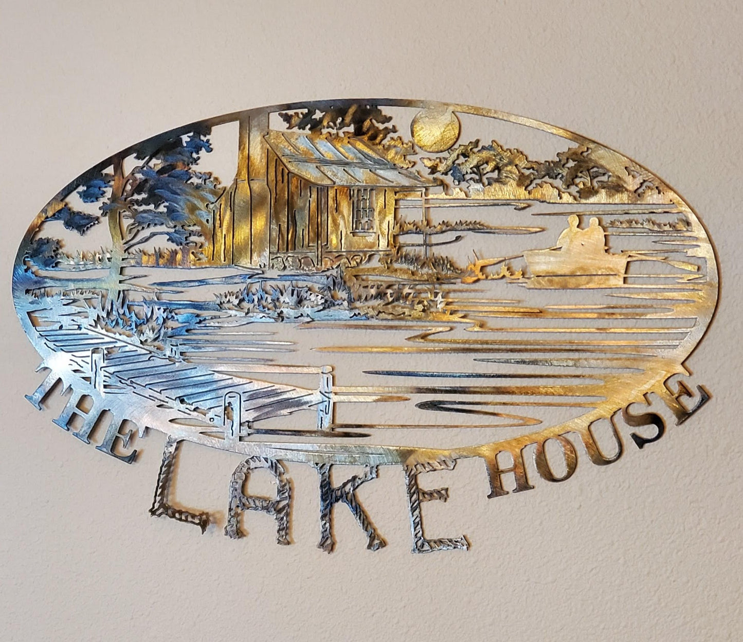 The Lake House Metal Wall Hanging features an old cabin in front of a river with a moon overlooking the scene. There's a boat with two people in the river. The word The Lake House is at the bottom. Made from 18-gauge cold rolled sheet metal. Available in four colors. Colored which looks very rustic looking, black, hammer tone, and bare metal. Sprayed with several layers of varathane. Can be used on porch if kept from rain and snow. Gift wrapping available at checkout.